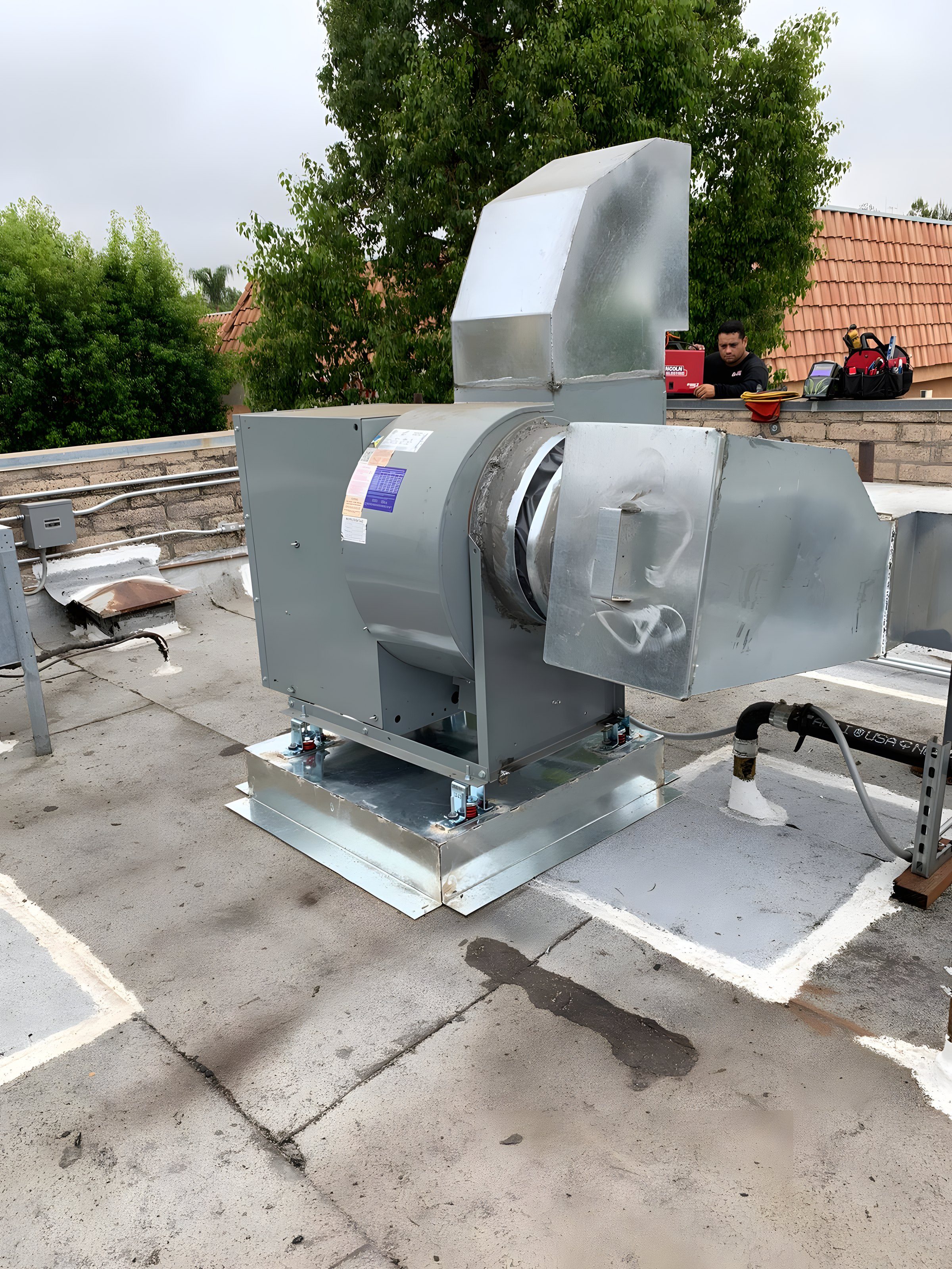 A technician at a rooftop kitchen exhaust fan